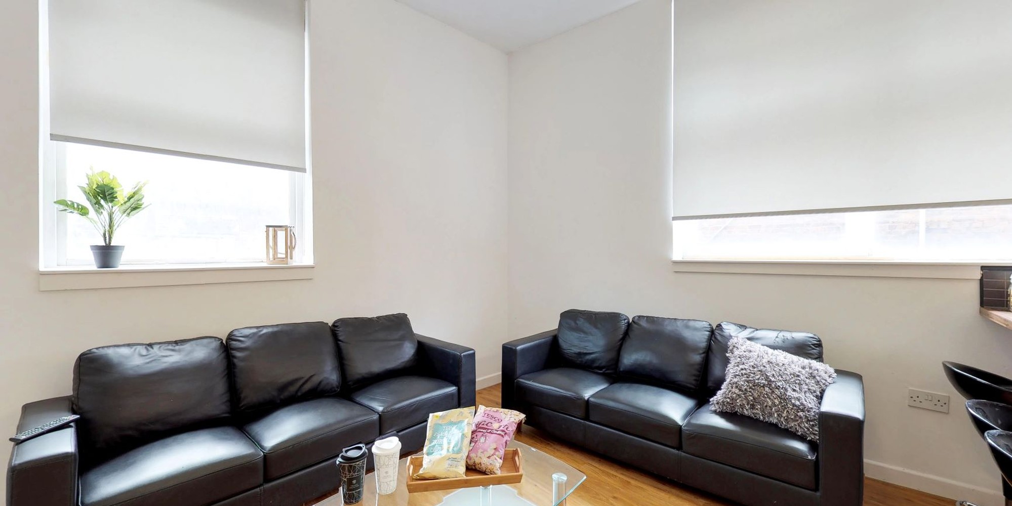 Big living room area at Haigh Court with 2 3-seated black leather sofas and a coffee table in the middle with crisps and popcorn.  